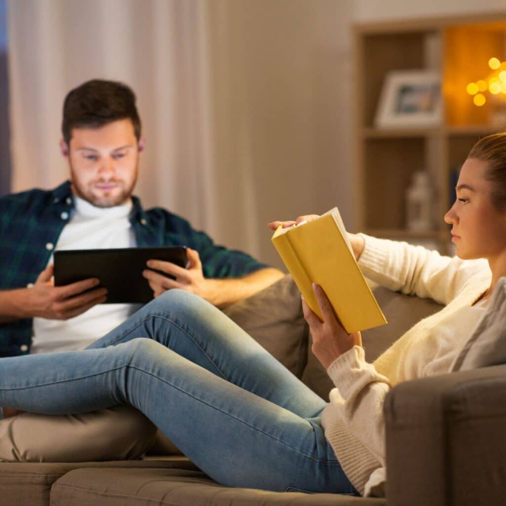 couple comfortable on their couch reading a book and looking at their tablet, comfortable because of heating services from hill and company