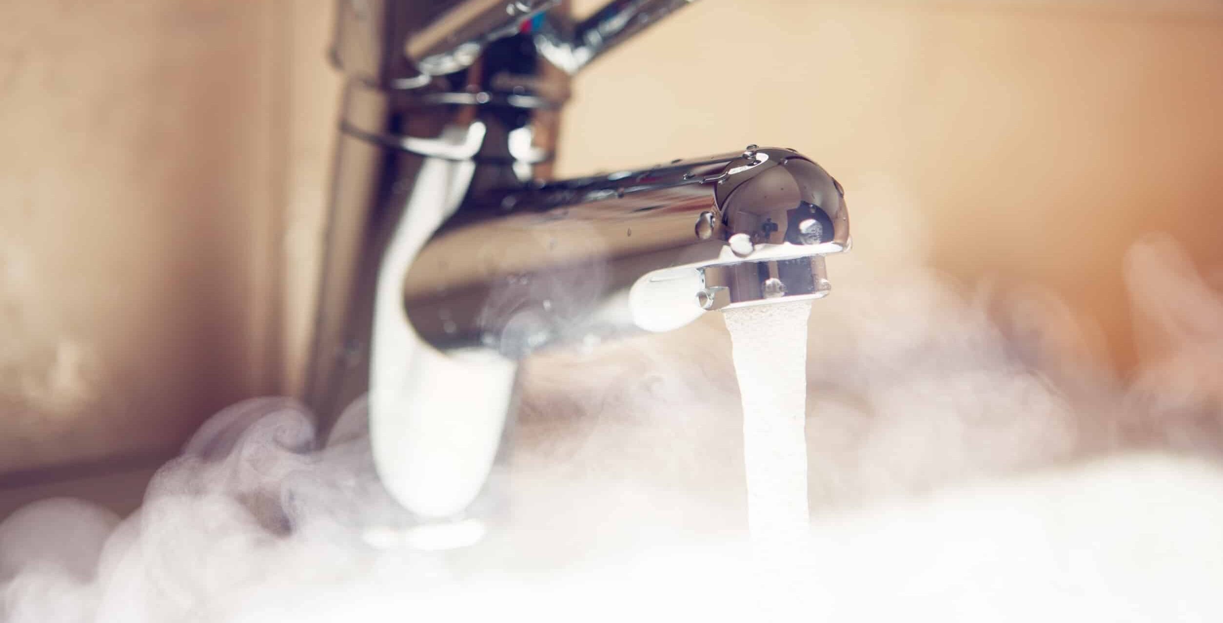 closeup of steaming hot water flowing from a silver bathroom sink faucet