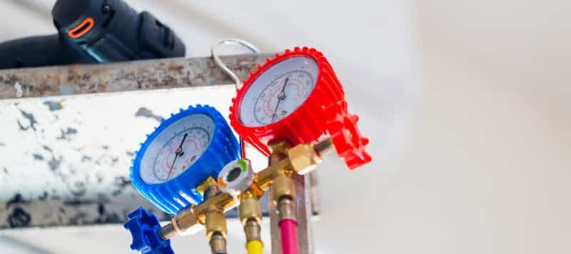 red and blue gauges reading the refrigerant levels on an ac unit