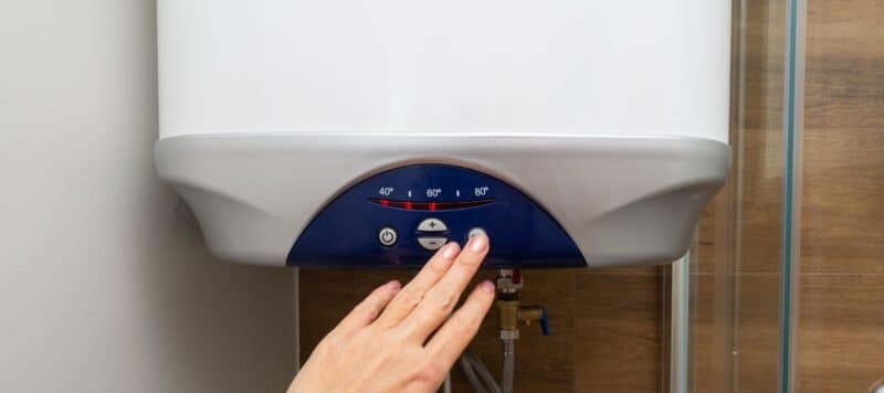 hand pressing button on blue and white tankless water heater to adjust the temperature settings