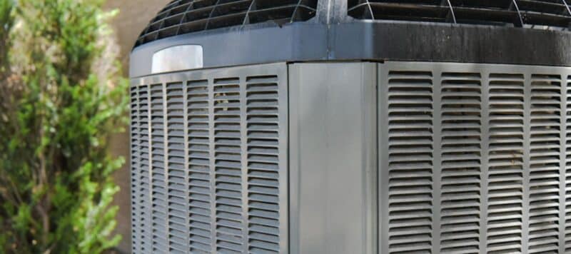 Close-up view of a residential air conditioning unit with surrounding shrubbery