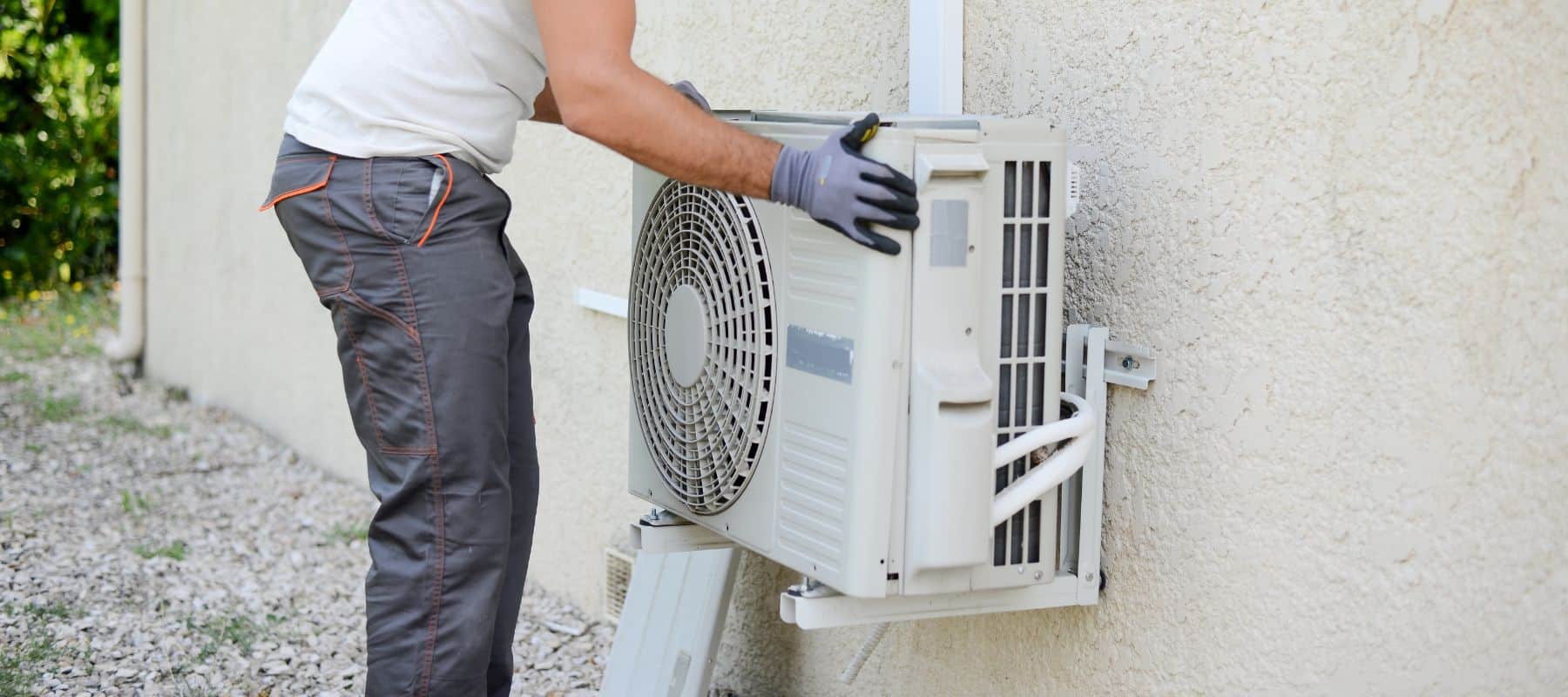 hvac technician wearing gloves installing an hvac unit on the outside of a house